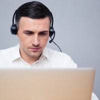 Businessman using laptop in headphones over gray background