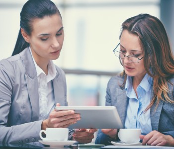 Image of two confident businesswomen working with touchpad in office